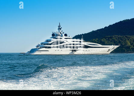 Grand luxury motor yacht croisières en mer à bord d'un océan calme passant un littoral boisé vue sur le sillage d'un navire de passage Banque D'Images