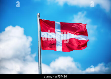 Drapeau national du Danemark voletant dans le vent sur un mât contre un beau ciel bleu avec des nuages blancs moelleux Banque D'Images