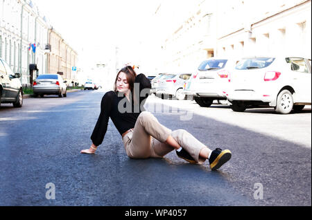 Belle jeune femme assise sur la chaussée dans la ville Banque D'Images