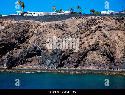 Couches de panneaux coulées avec des tubes et des grottes près de la Lanzarote resort de Puerto del Carmen. Rock de basalte noir de l'Atlantique d'Azur Banque D'Images