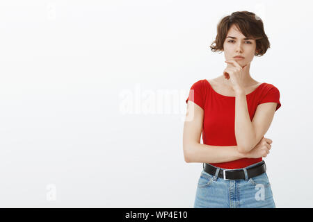 Hmm pas sûr de dire la vérité. Jeune femme sérieuse suspectes porté courte coupe pixie loucher incertaine rub chin pense réfléchir ou de fiducie Banque D'Images