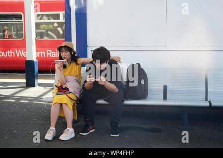 Un jeune couple à la recherche de leur téléphone sur un quai de gare. Banque D'Images