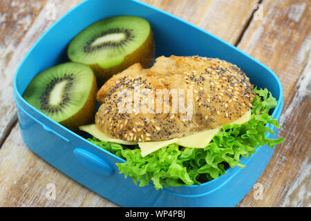 Rouleau complet avec du fromage et de la laitue avec deux moitiés de kiwi en bleu lunch box Banque D'Images