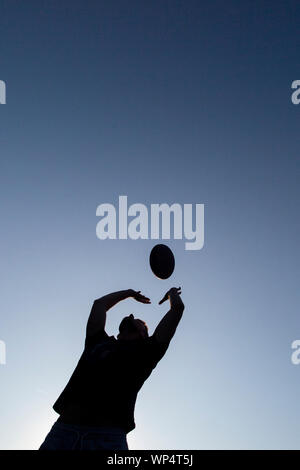 Un garçon prendre et transmettre un ballon de rugby sur une journée d'été dans un parc, de formation pour la nouvelle saison Banque D'Images