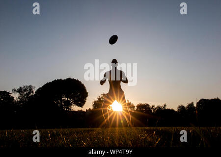 Un garçon prendre et transmettre un ballon de rugby sur une journée d'été dans un parc, de formation pour la nouvelle saison Banque D'Images