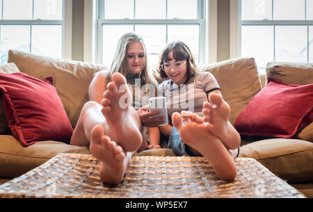 Deux adolescentes assis sur table avec les pieds jusqu'à la au téléphone cellulaire. Banque D'Images