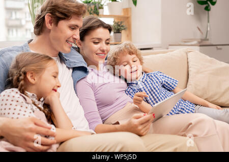 Cute boy pointing at tablet écran tout en regardant des dessins animés avec la famille Banque D'Images