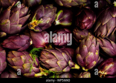 Bande d'artichauts violets au hasard en tas à un marché de producteurs Banque D'Images