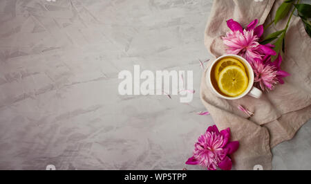Vue de dessus d'une tasse de thé avec des fleurs roses sur la surface grise. Banque D'Images