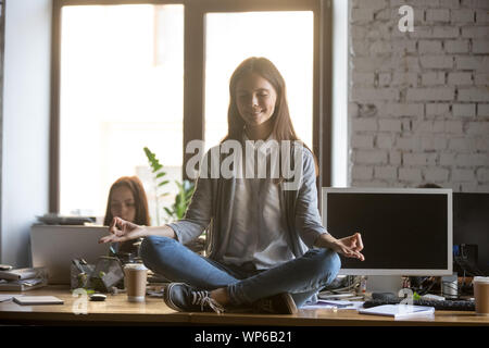 Smiling young businesswoman meditating, pratiquer le yoga sur office 24 Banque D'Images