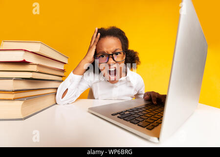 Élève d'école élémentaire fille assise à l'ordinateur portable et crier en Studio Banque D'Images