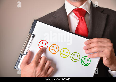 Homme en costume cravate avec un visage en colère montrant un émoticône dessinée sur une feuille. Composition horizontale. Vue avant Banque D'Images