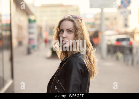 Serious attractive curly blonde en blouson de cuir standing on city street at over shoulder Banque D'Images