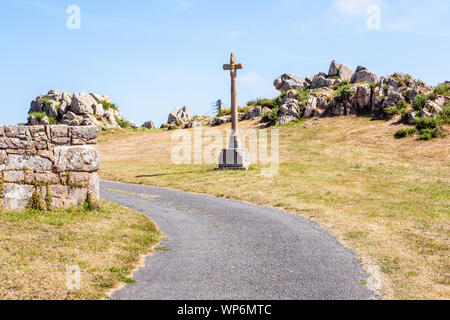 Calvaire de granit en Bretagne, France, sur le flanc d'une petite route en face d'un affleurement de granit sur une journée ensoleillée. Banque D'Images