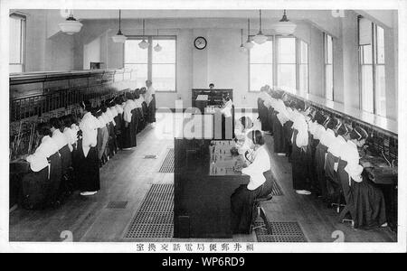 [ 1920 - Japon ] Centre de commutation téléphonique japonais - Des dizaines de jeunes femmes en uniforme au travail à un tableau de Fukui centre de commutation téléphonique Yubinkyoku (bureau de poste). Fukui Yubinkyoku a été créée le 8 avril 1872 (5) l'ère Meiji. Le Japon a importé en 1877 son premier téléphone de Meiji (10). Les opérateurs téléphoniques ont été appelé Bonjour les filles (ハローガール). 20e siècle vintage carte postale. Banque D'Images