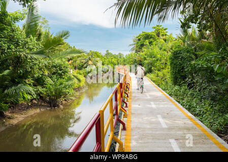 Un jeune homme en cycles (Krachao Bang Bang Kachao), le long de la douve et voie surélevée entourée par une végétation tropicale. Banque D'Images