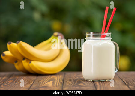 Smoothie banane en pot Mason sur table en bois avec fond naturel Flou vert Banque D'Images