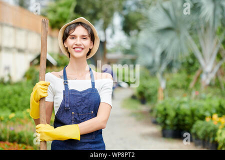 Portrait of pretty smiling woman in hat standing et globale avec spade ou Peigne manche bois de jardin Banque D'Images