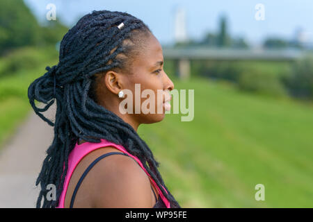 Profil d'un young African woman wearing hair extensions tresses en fixant sur campagne verdoyante avec une expression grave Banque D'Images