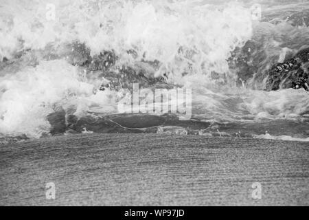 Après-midi forte marée, marée avec des vagues se brisant sur les rochers sur les rochers avec de fortes vagues écumeuses, un ressac, un lavage du côté en noir & blanc Banque D'Images