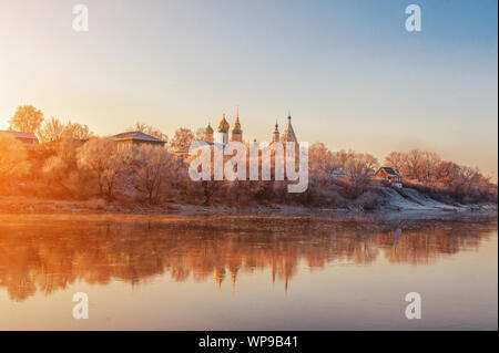 Paysage d'hiver des temples de la ville avec coucher de soleil sur la rive de la rivière. Les arbres sont couverts de neige, le soleil couchant illumine un beau Banque D'Images