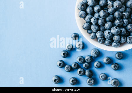 Close-up d'une plaque avec les bleuets et baies à proximité sont dispersées sur un fond bleu. Source de vitamines et de régime alimentaire. Banque D'Images