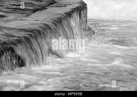 Abstrait noir et blanc des photographies d'un paysage marin avec de forts remous avec de l'eau coulant sur un bassin de marée mur à une faible vitesse d'obturation - puissant Banque D'Images