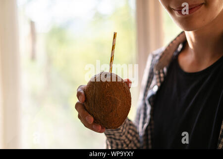 Jeune homme tenant la noix de coco avec une paille et boire, Close up Banque D'Images