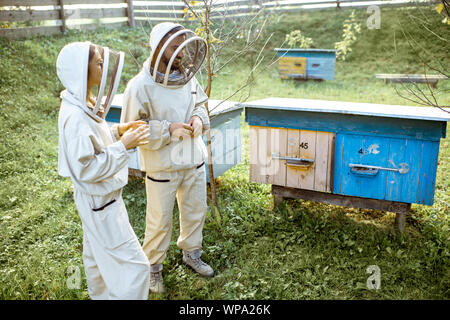 Deux jeunes en beekepers de travail uniformes de protection sur une petite ferme avec des ruches en bois rucher sur l'arrière-plan Banque D'Images