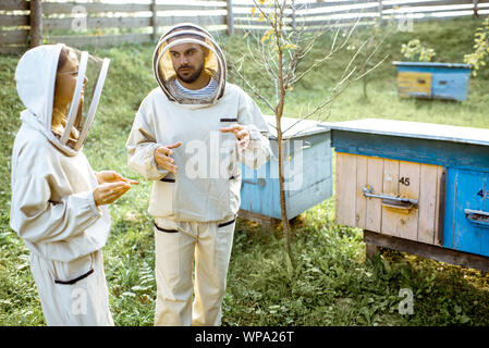 Deux jeunes en beekepers de travail uniformes de protection sur une petite ferme avec des ruches en bois rucher sur l'arrière-plan Banque D'Images