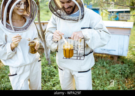 Deux beekepers uniforme de protection en se tenant ensemble avec du miel dans le pot, dégustation de produits frais sur le rucher en plein air Banque D'Images