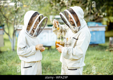 Deux beekepers uniforme de protection en se tenant ensemble avec du miel dans le pot, dégustation de produits frais sur le rucher en plein air Banque D'Images