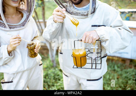 Deux beekepers uniforme de protection en se tenant ensemble avec du miel dans le pot, dégustation de produits frais sur le rucher en plein air, close-up view Banque D'Images