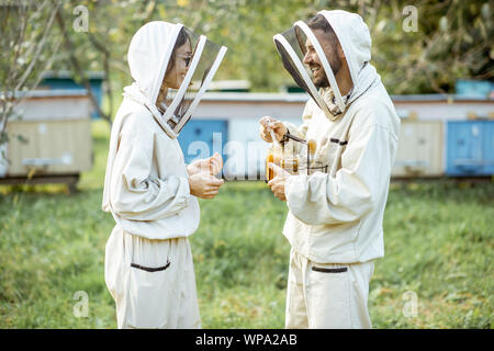 Deux beekepers uniforme de protection en se tenant ensemble avec du miel dans le pot, dégustation de produits frais sur le rucher en plein air Banque D'Images