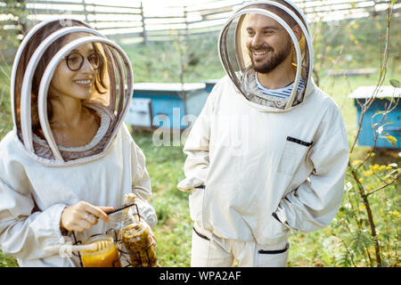 Deux jeunes en beekepers de travail uniformes de protection sur une petite ferme avec des ruches en bois rucher sur l'arrière-plan Banque D'Images