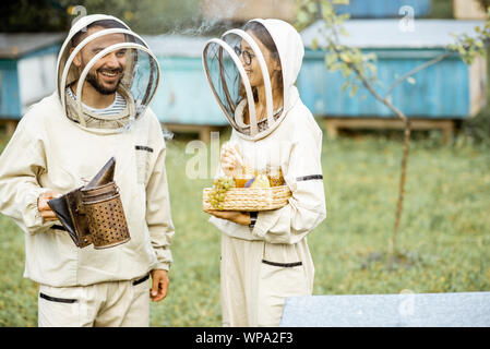 Deux beekepers en uniforme de protection avec beesmoker permanent et du miel, dégustation de produits frais sur le rucher Banque D'Images