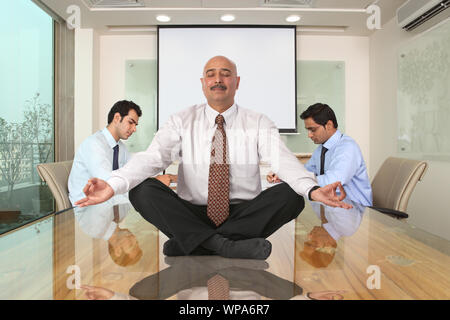Homme d'affaires assis dans le yoga pose sur table Banque D'Images