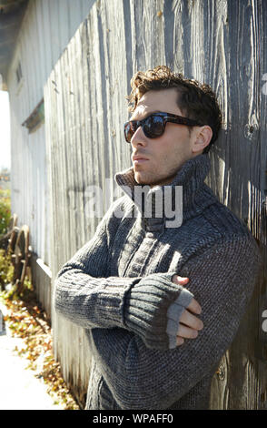 Bel homme à lunettes en pull-over chaud leaning on barn Banque D'Images