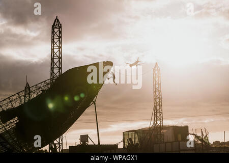 L'homme l'ascension d'une grande antenne satellite pendant le coucher du soleil Banque D'Images