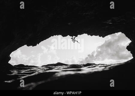 L'escalade de l'homme au-dessus de l'océan dans une grotte volcanique Banque D'Images