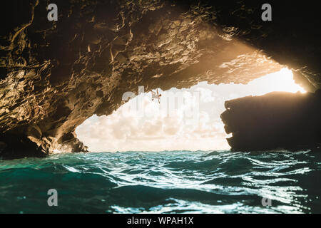 L'escalade de l'homme au-dessus de l'océan dans une grotte volcanique pendant le coucher du soleil Banque D'Images