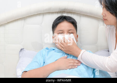 Image enfant asiatique malades ou de nettoyage essuyer le nez avec un mouchoir alors que mère de l'aider. Les soins de santé, la fièvre et la grippe concept. Banque D'Images