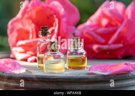 Bouteilles d'huile essentielle avec des fleurs rose à l'arrière-plan Banque D'Images