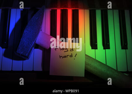 Un marteau avec une note disant "jouez à disque, repose sur un clavier du piano dans la lumière. Banque D'Images