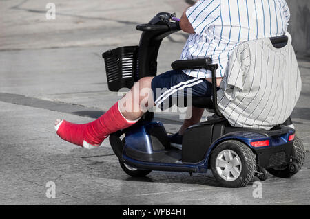 L'homme avec l'aide de la jambe blessée mobilty scooter sur vacances en espagne Banque D'Images