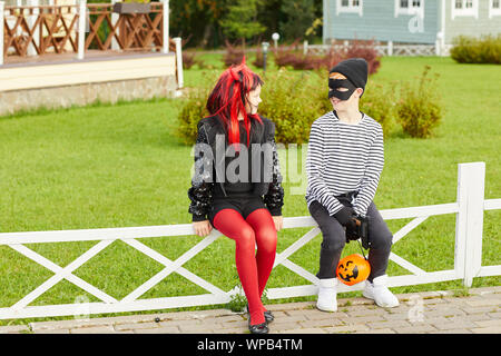 Portrait de deux heureux petits enfants portant des costumes de Halloween sitting on fence tandis que tour ou traitement, copy space Banque D'Images