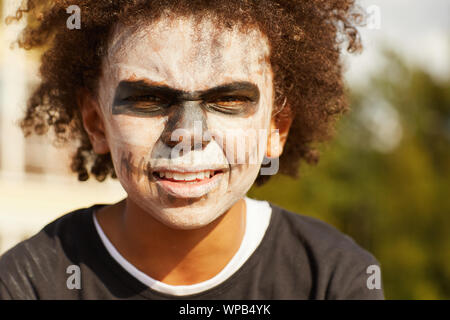 Head and shoulders portrait of boy wearing afro-américaines difficiles costume squelette posant à l'extérieur sur l'Halloween, éclairée par la lumière du soleil Banque D'Images