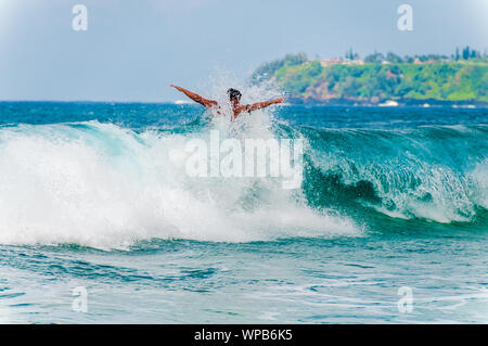 Jeune homme monté sur une planche de surf dans une vague bleue à l'été. Banque D'Images