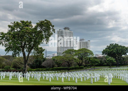 Manille, Philippines - Le 5 mars 2019 : American Cemetery and Memorial Park. Pelouse verte, des croix blanches et des nuages. Gratte-ciel blanc sur l'horizon. Banque D'Images