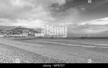 Une vue de la rive et courbée du Llandudno pier. Le grand orme pointe est dans la distance et un ciel nuageux est ci-dessus. Banque D'Images